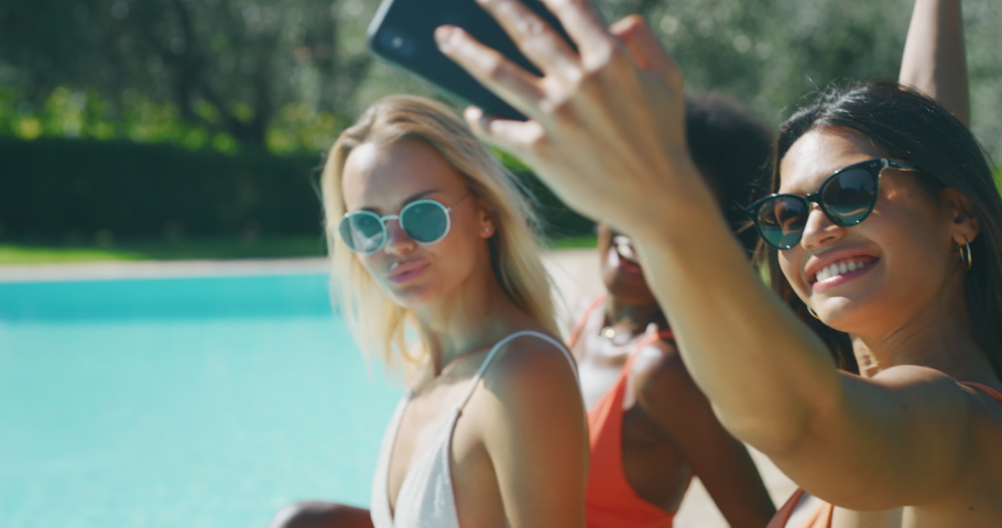 Slow motion close up of young multi-ethnic girlfriends with sunglasses in swimwear are having fun to enjoy their summer vacation together and taking a selfie in swimming pool  in a sunny day. Royalty-Free Stock Footage #1037475314