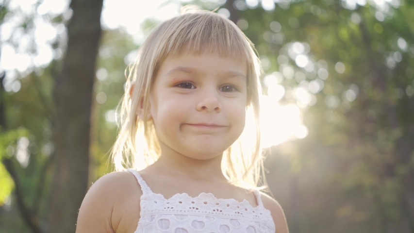 Close-up of a little cute girl looking at the camera and pointing away. Portrait of bautiful child in the park in sun rays.