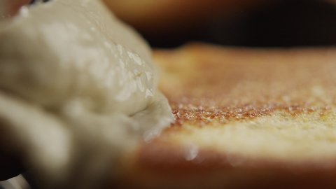 Macro shot of man with knife spreading cream cheese on toast. Slow motion video