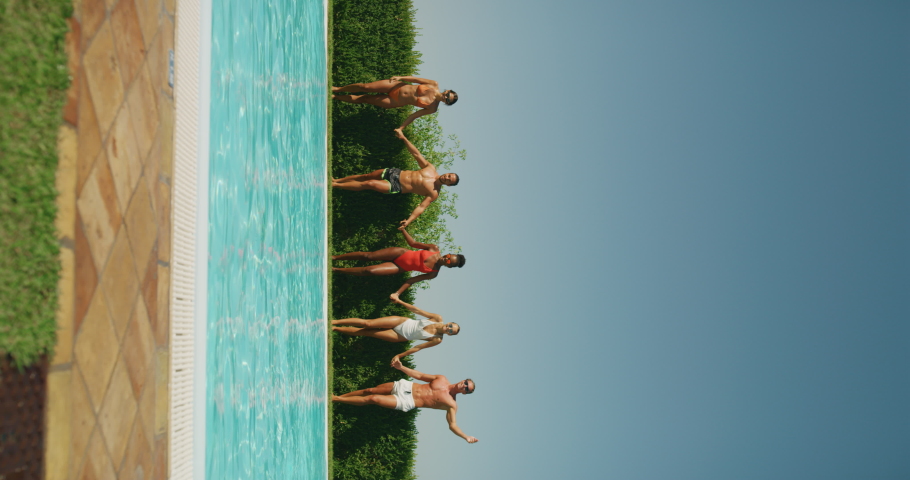 Vertical shot of young multi-ethnic friends in swimwear are having fun to enjoy their summer vacation together and jumping in a water in swimming pool in a sunny day.
