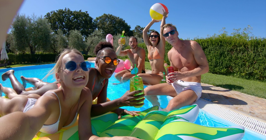 Authentic shot of young multi-ethnic friends in swimwear are relaxing on colorful inflatables and making a selfie or video call with a smartphone in swimming pool in a sunny day.