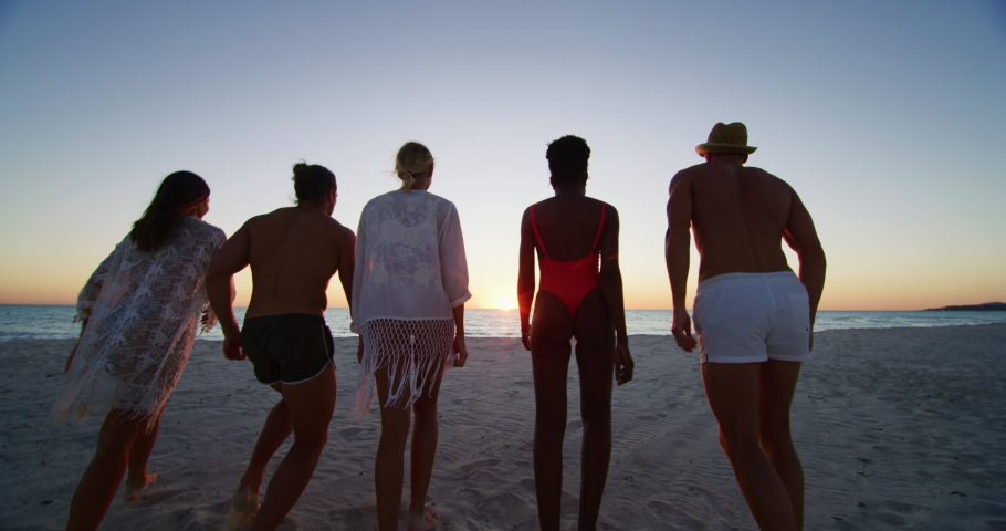 Slow motion of young multi-ethnic carefree  friends in swimsuits are having fun and enjoying their summer vacation together on a beach with a sea on a sunset.