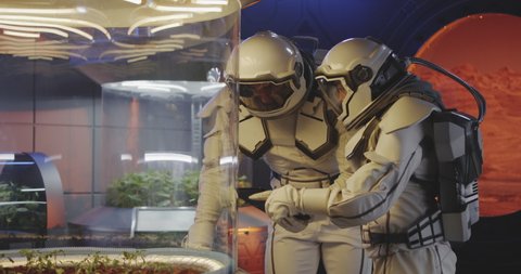 Medium shot of two astronauts examining plant incubators on a Mars base