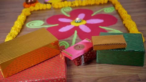 Bokeh shot of a beautiful rangoli with colorful gift boxes on the occasion of Diwali. Tilt shot of a Diwali rangoli decorated by flowers, gifts, Kalash, mango leaves, coconut, an oil lamp, and a fe...