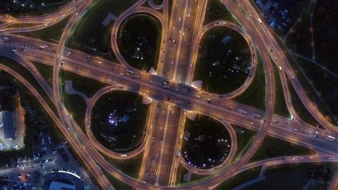 Helicopter epic round road junction with a night beautiful pattern of illuminated modern Moscow urban roads. Traffic intersection in metropolis. Many cars travel fast directions. Lift up altitude 4K