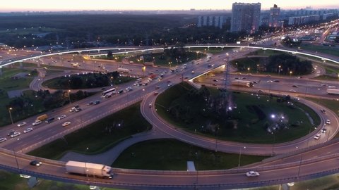 Huge clover road junction at sunset backlight highway track active movement of cars buses. Cinematic cityscape of freeway goes deep into city. Moscow capital Russia modern metropolis. Aerial climb