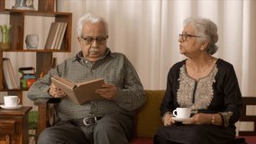 Clip of Indian wife interrupting husband while he is reading. HD video clip of an old Indian husband reading a book while his old wife disturbs. A scene of a typical Indian family day to day routine