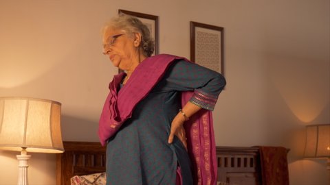 Shot of an old Indian woman having back pain. Indian stock footage of a senior woman having pain in back while getting up from her bed