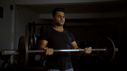 A muscular and fit Indian man doing barbell curl (bicep) exercise in the gym.