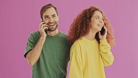 Handsome cheerful young couple smiling and having a call on their smartphones over pink background isolated