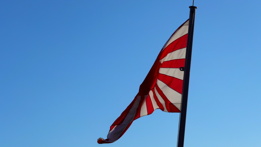 
Japan's naval flag unfolds in the wind. Japan flag swaying in the wind on an end day against a blue clear sky