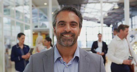 Portrait of a middle aged mixed race businessman looking to camera and smiling, standing in a conference foyer with a group of business people talking in the background