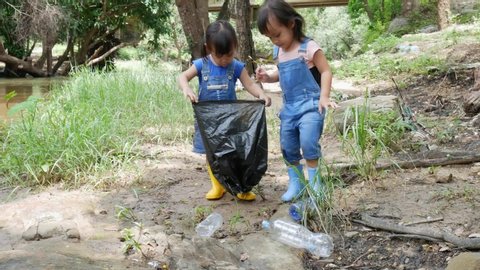 Asian little children is picking up garbage and plastic bottle in black bags on the edge of a public river. Environmental protection concept.
