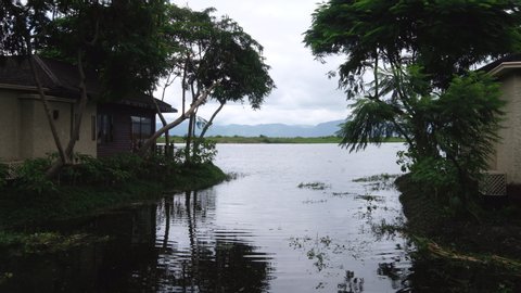 Inle lake between green trees and houses in Myanmar. Rippled lake water. White cloudy sky and mountains