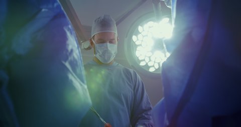 Low angle view of Caucasian male surgeon performing operation in operation theater at hospital. He is using surgical scissor. Healthcare workers in the Coronavirus Covid19 pandemic
