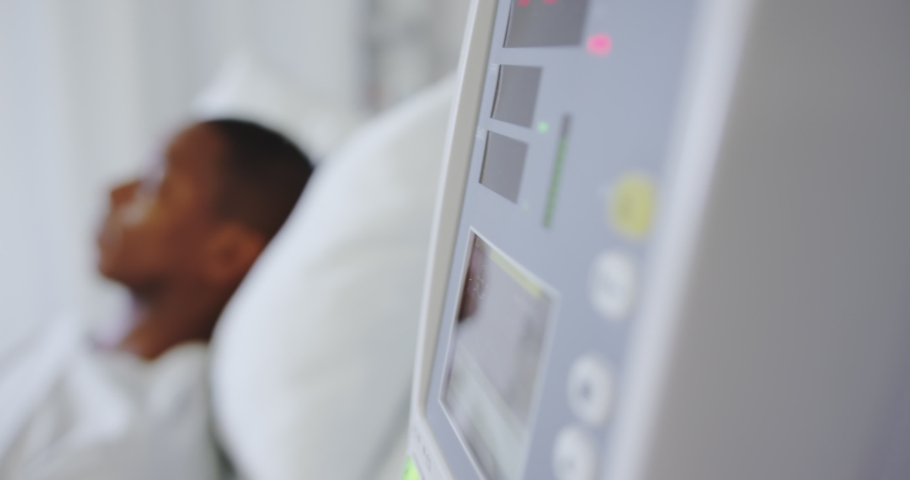Close-up of medical monitor with African american male patient in the ward at hospital. Digits blinking on monitor. Healthcare workers in the Coronavirus Covid19 pandemic Royalty-Free Stock Footage #1037506490