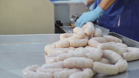Production worker in blue rubber gloves, makes sausage. A close-up of a sausage is created by an employee