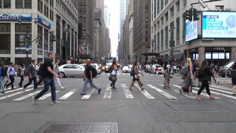 New York City - Circa 2019: Pedestrians cross busy 7th avenue crosswalk in Manhattan during morning commute in slow motion. View uptown towards Times square. Famous Macys store on street corner