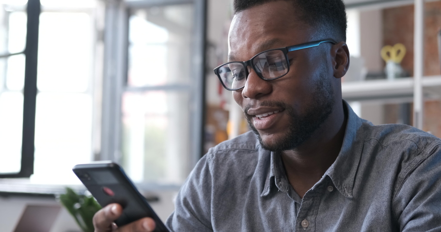 African american man in glasses holding smartphone and having video chat in modern office. Man having video chat smiling on a smartphone. Enjoying communicating on mobile phone connection. Close up | Shutterstock HD Video #1037523047