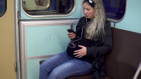A pregnant woman is listening to music on headphones in a subway train. Old subway train car