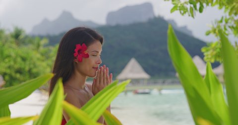Spiritual Namaste Yoga Meditation Hand Gesture Woman On Meditating Retreat on Beach in Luxury Hotel Vacation Holidays. Multiracial female model with flower in hair on tropical travel. SLOW MOTION RED.