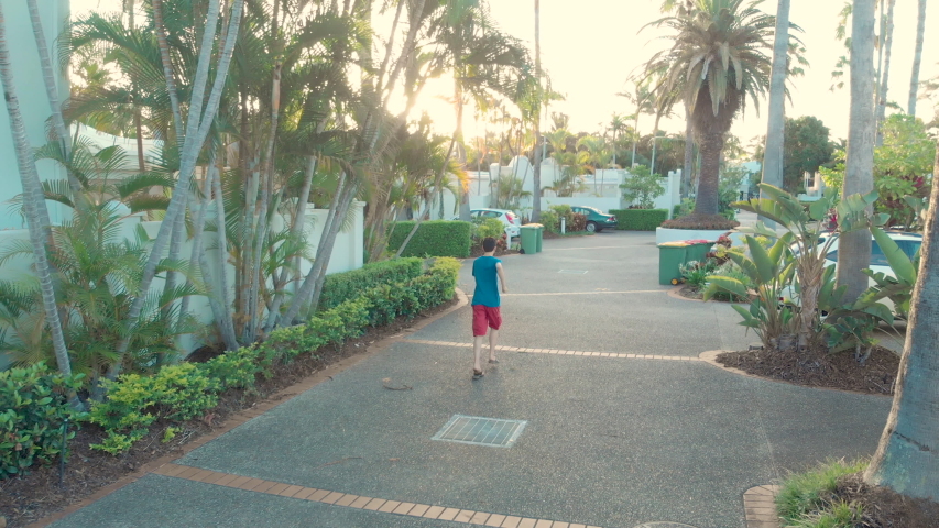 AERIAL: Teenager jogging forward through street during sunset