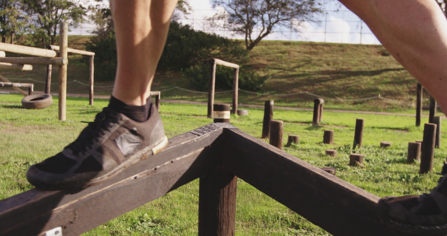 Side view low section of a young Caucasian man walking along a beam at an outdoor gym during a bootcamp training session in slow motion Royalty-Free Stock Footage #1037532434