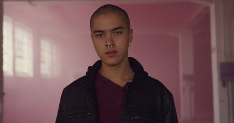 Portrait of a hip young mixed race man in an empty warehouse, looking to camera surrounded by pink smoke from a hand grenade