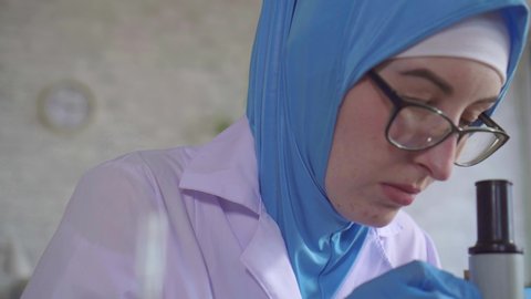 Muslim woman chemist scientist in national scarf working with microscope in laboratory close up