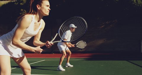 Side view of a young Caucasian woman and a young Caucasian man playing tennis on a court, man returning a ball