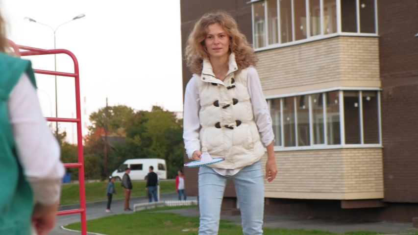 Beautiful little preschool girl with long wavy hair in mint-colored clothes with her mother plays badminton in the summer on a children