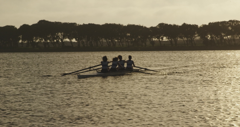 Rear view of a team of four young adult Caucasian women rowing in a racing shell on a river