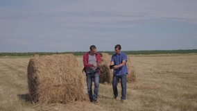 teamwork agriculture smart farming concept. two men workers farmers walking studying haystack in field on digital tablet. teamwork slow motion video. people agronomist botanist farmers working in