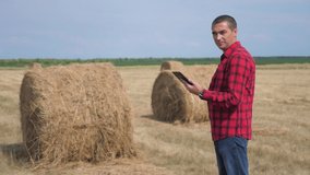 smart farming agriculture concept. man farmer worker studying a haystack in a field on digital tablet. slow motion video. male agronomist botanist farmer working lifestyle in the field