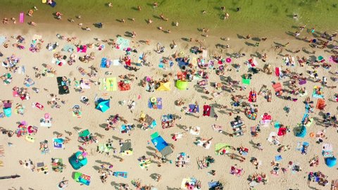 Aerial view of waves crashing on the beach with people and umbrellas on the shore on a beautiful summer day.