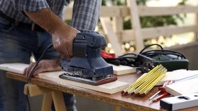Adult carpenter craftsman with electric sander smoothes a wooden table. Housework do it yourself. Footage.