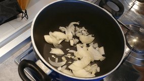 Adding wine to a cooking pot filled with diced onions and garlic cloves, full HD, 24 fps