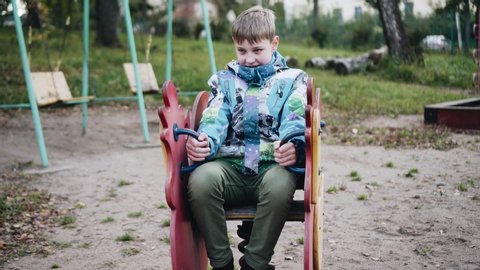 The boy sits on a wooden chair on a spring and swings. Funny funny moment. Good mood