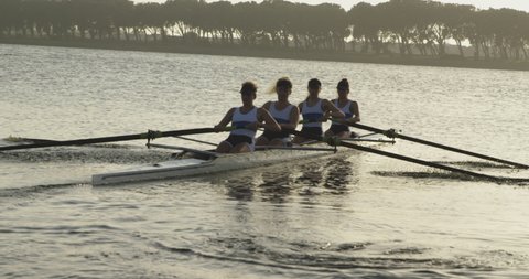 Front view of a team of four young adult Caucasian women rowing in a racing shell training on a river in slow motion