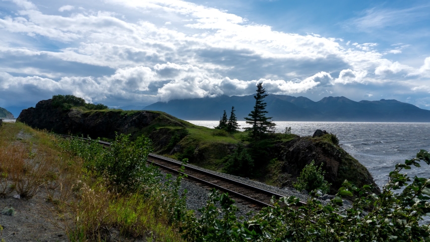 Scenic Alaska fjord surrounded by mountains and trees with blue skies and white clouds.