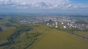 Aerial view of field with trees near the industrial area located outside the city. Clip. Amazing view of factories tanks and tank farm for bulk petroleum and gasoline storage