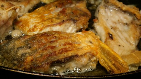 Homemade kitchen. River fish carp, cut into pieces, is fried in pan in cooking oil. Close-up.