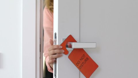 Young woman hanging do not disturb sign and closing door, privacy in hotel