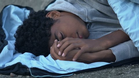 Freezing African-American refugee lying on street in sleeping bag, hopelessness