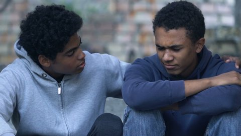 Afro-American teen boy with bruised face hugging brother sitting alone on stairs