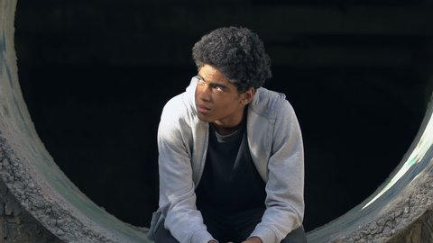 Upset mixed-race teen boy sitting alone in abandoned lane, lack of communication
