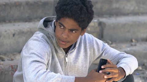 Sad afro-american teen scrolling smartphone, feels nervous, awkward age problems