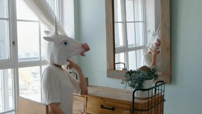 Strange funny video: woman in a mask of unicorn looking in the mirror in bedroom