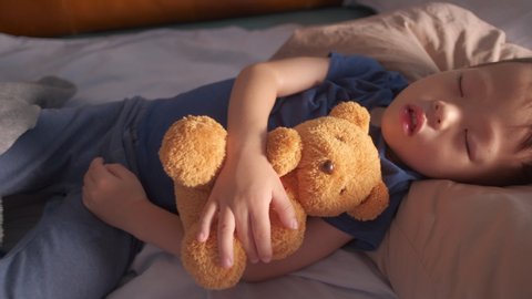 Cute little Asian 3 - 4 years old toddler boy kid sleeping / taking a nap in bed while hugging teddy bear, kid deep sleeping, sweet dream concept