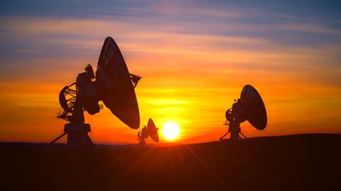 Three large radio telescope antennas against scenic sunset sky raise its dishes up exploring evening sky. Radio telescopes are used in science for space observation and distant objects exploring.